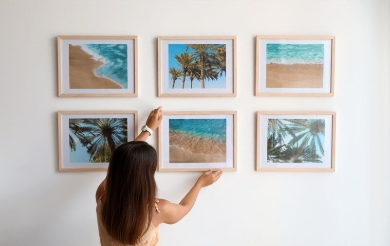 A woman adjusts one picture frame out of a group hanging on a wall together