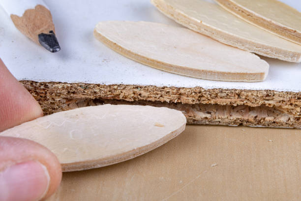 a hand slides a joinery biscuit into a groove and the end of a board