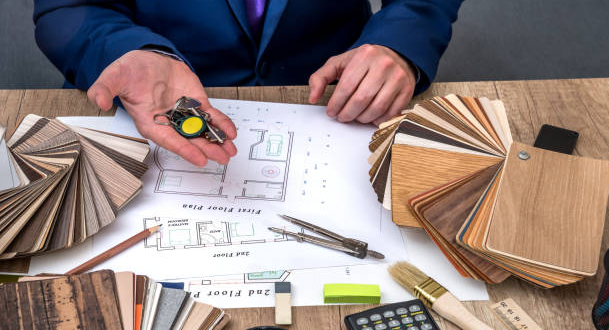 an individual sits at a desk with blue prints, design tools, and wooden swatches